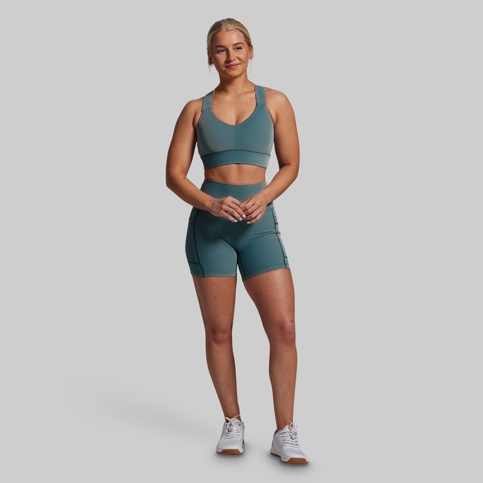 Woman wearing a green sports bra and shorts set on a gray background