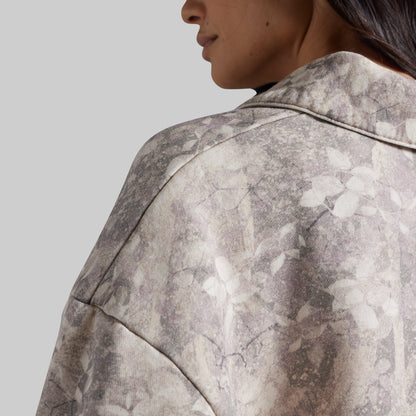 Close-up of a person wearing an abstract-patterned sweatshirt in muted gray, beige, and off-white tones, shown from the side against a plain light gray background.