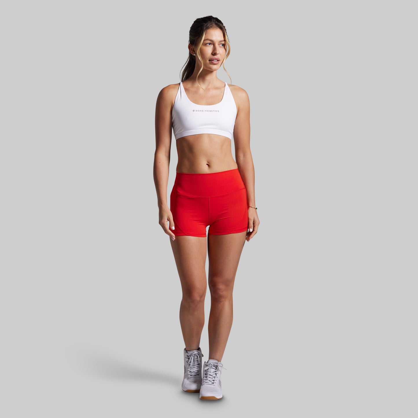 Woman wearing a white sports bra and red shorts on a gray background