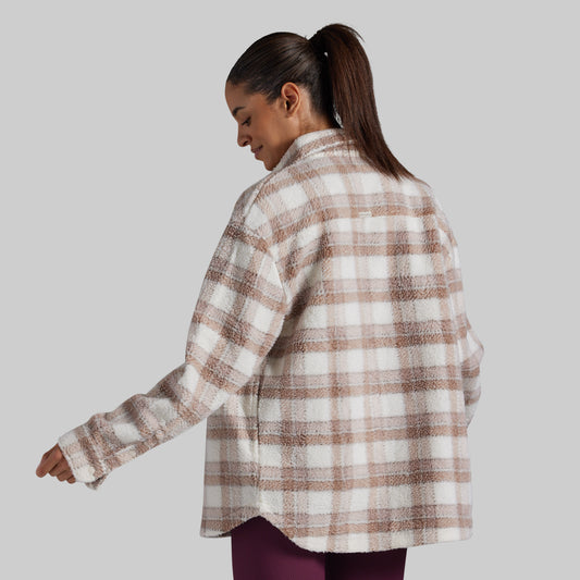 A woman wearing an oversized, long-sleeve plaid fleece button-up shirt in beige and white, shown from a three-quarters back view against a solid gray background.