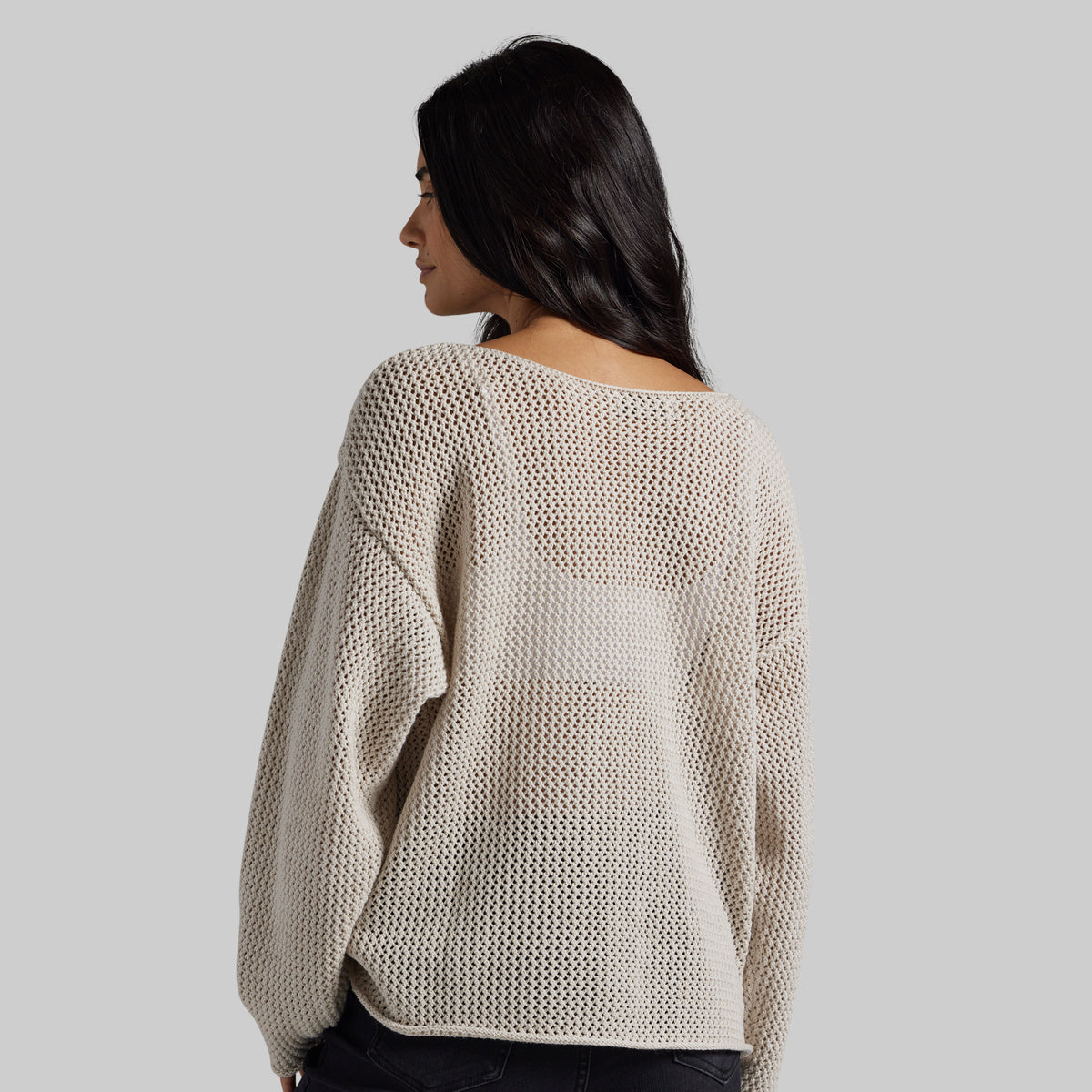A woman shown from the back wearing a cream-colored, textured knit sweater with a wide boat neckline, set against a solid light gray background.