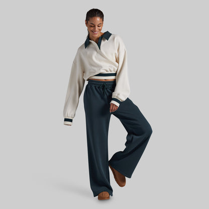 A woman modeling a cream long-sleeve collared sweatshirt with dark green trim and matching dark green wide-leg drawstring pants, paired with brown shoes, against a solid light gray background.