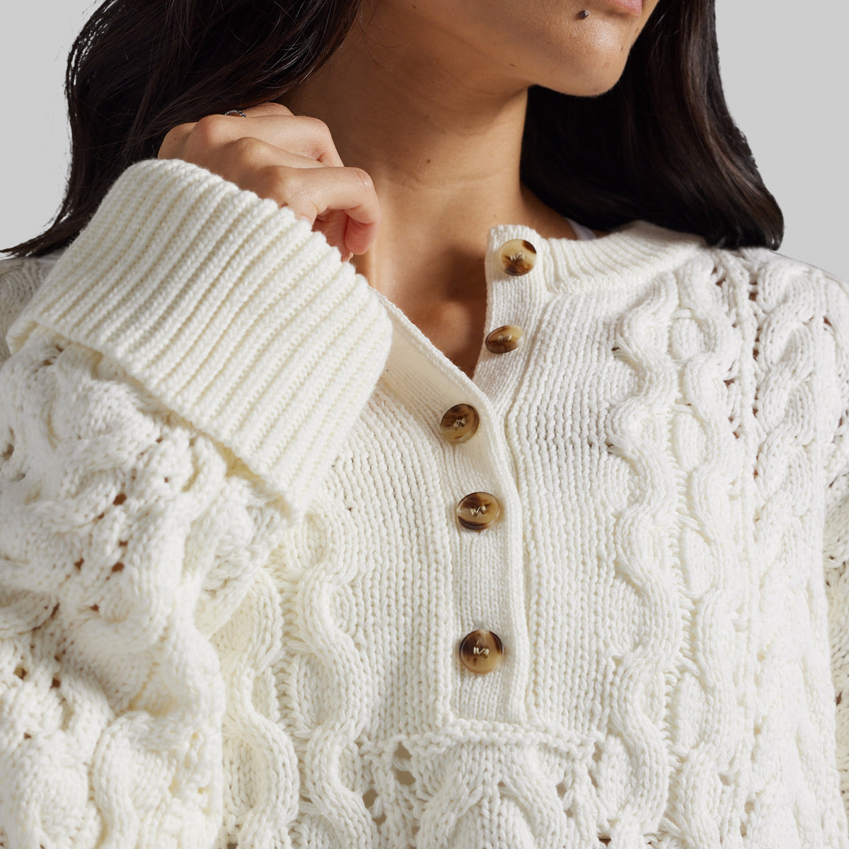 Close-up of a woman wearing a cream cable-knit sweater with a buttoned henley-style neckline and brown buttons.