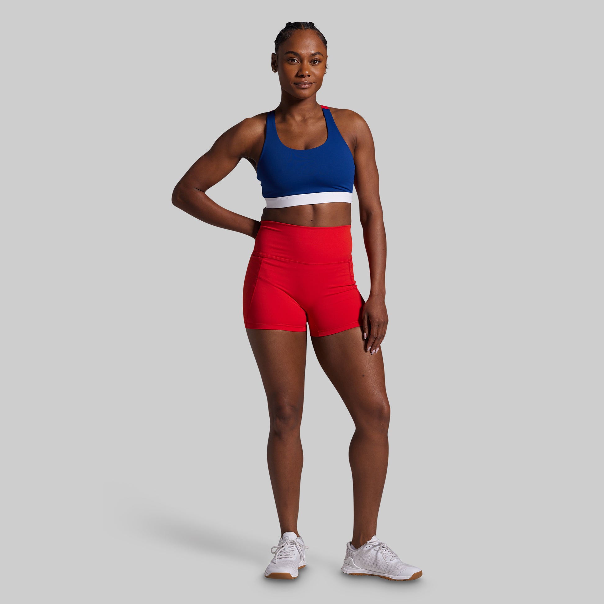 Woman wearing a blue sports bra and red shorts on a gray background