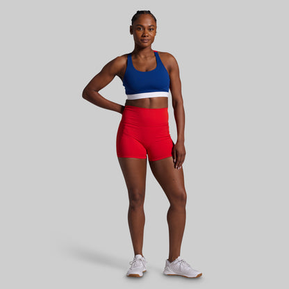 Woman wearing a blue sports bra and red shorts on a gray background