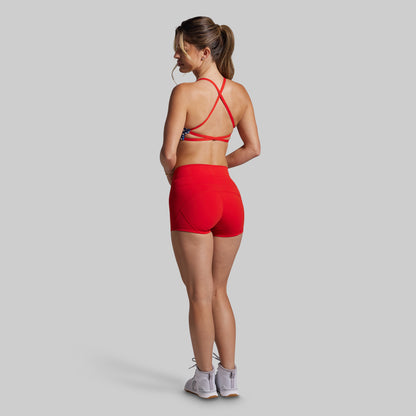 Woman wearing a red sports bra and shorts on a gray background