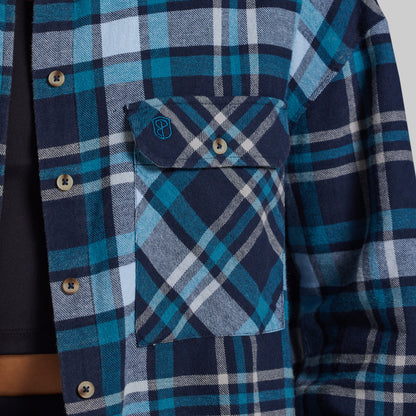 Close-up of a blue and navy plaid flannel shirt with a chest pocket and snap-button flap, worn over a dark undershirt.