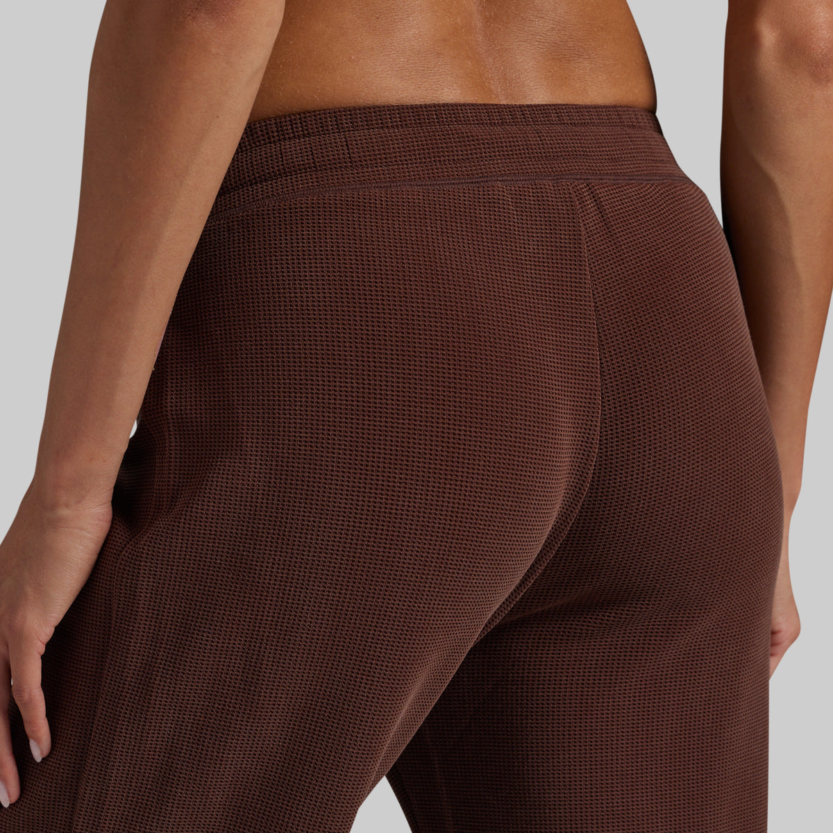 Close-up back view of a person wearing textured brown lounge pants against a light gray studio background.