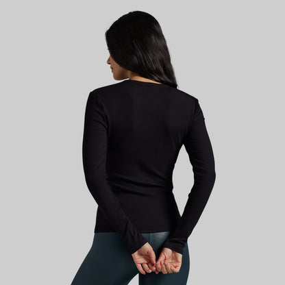A woman shown from the back wearing a fitted black long-sleeve top and dark leggings against a plain light gray studio background.
