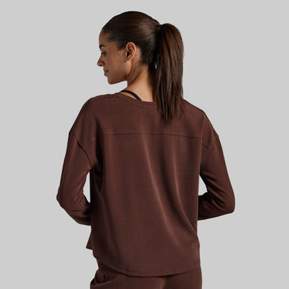 A woman is shown from the back wearing a dark brown long-sleeve top and matching pants against a solid gray background.