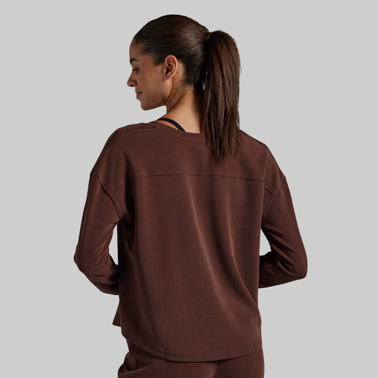 A woman is shown from the back wearing a dark brown long-sleeve top and matching pants against a solid gray background.