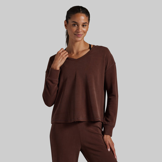 A woman modeling a matching brown lounge set consisting of a long-sleeve cropped V-neck top and coordinating pants, photographed against a solid light gray background.