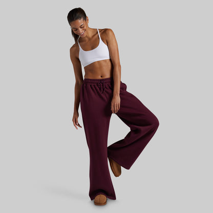 A model wearing wide-leg lounge pants in deep burgundy, paired with brown suede slippers