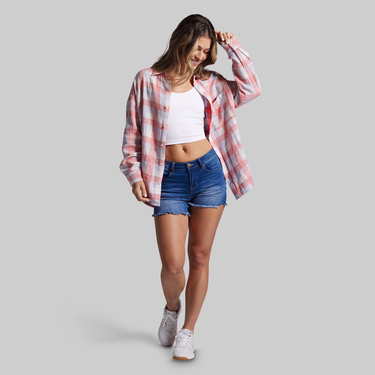 Woman wearing a plaid shirt, white top, and denim shorts on a gray background