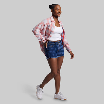 Woman wearing a plaid shirt, white top, denim shorts, and white sneakers on a gray background