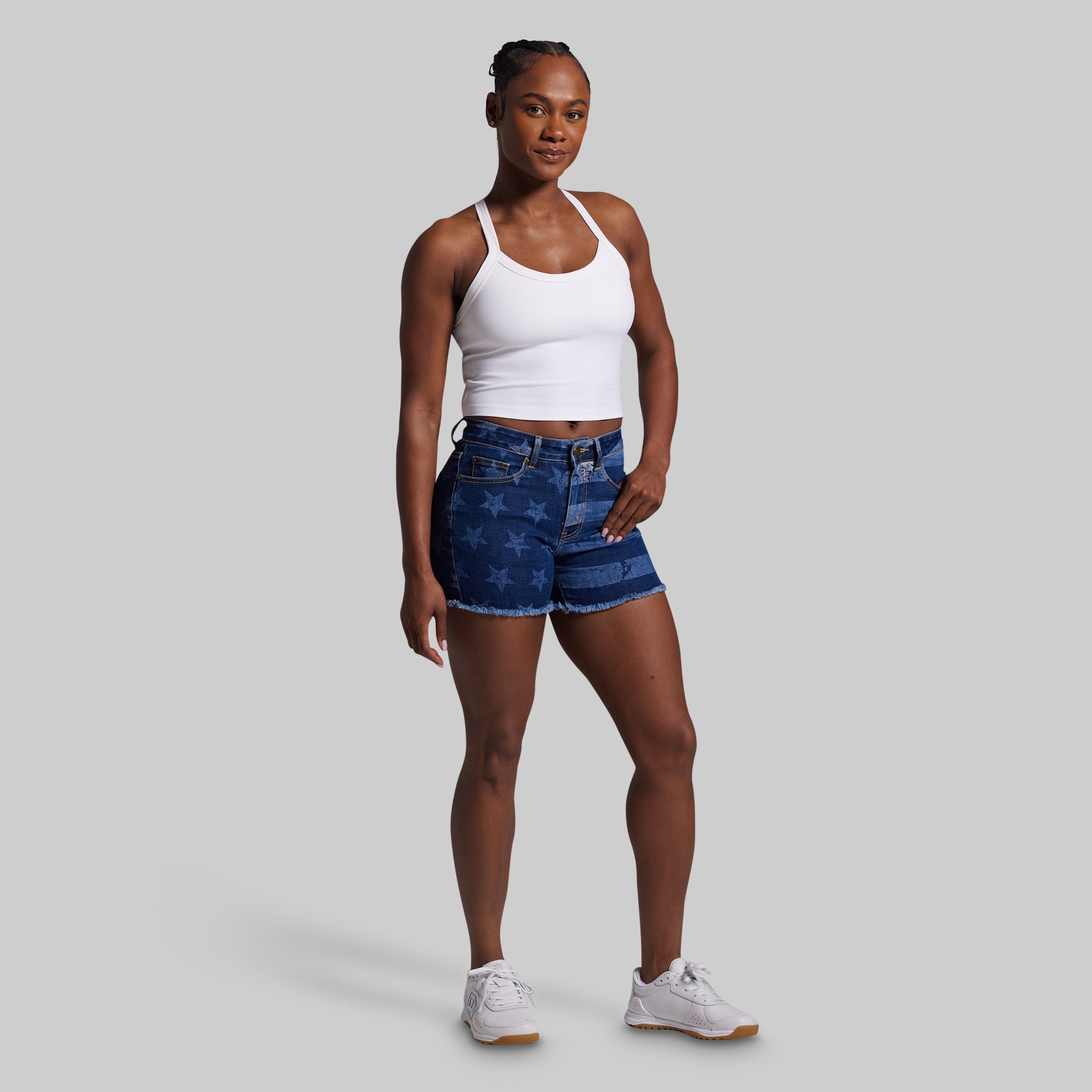 Woman wearing a white tank top and blue denim shorts on a gray background