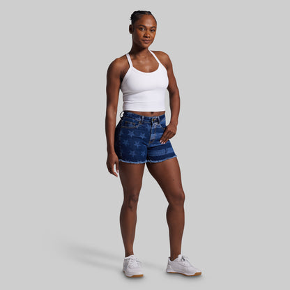 Woman wearing a white tank top and blue denim shorts on a gray background