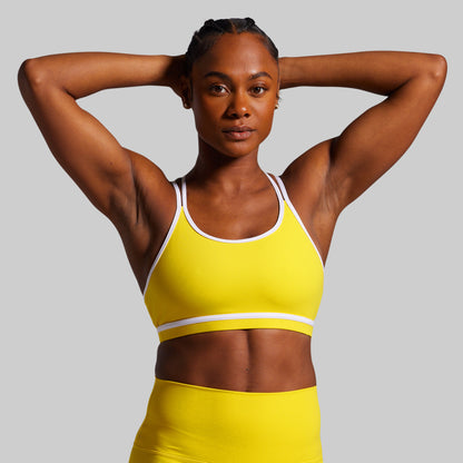 Woman wearing a yellow sports bra and shorts against a gray background