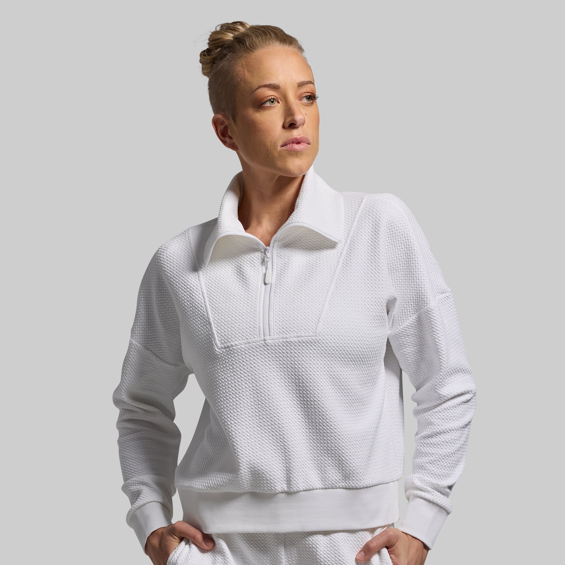 Woman wearing a white quarter-zip sweatshirt against a gray background