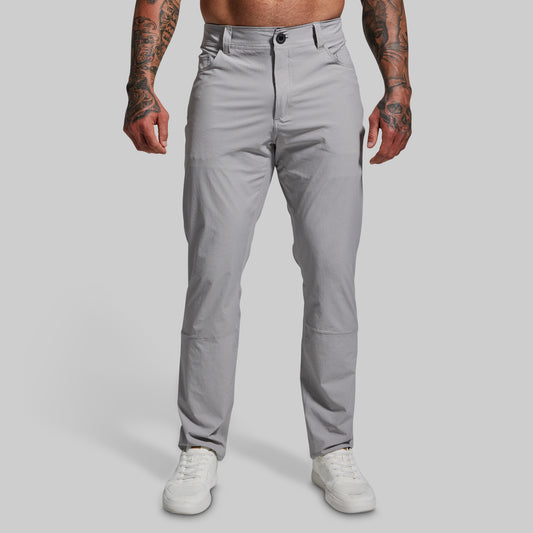 A male model wearing a pair of gray Traverse Pants with a button-and-fly closure, front pockets, and a regular fit.
