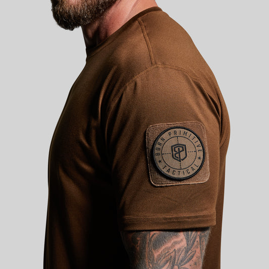 Person wearing a brown tactical shirt with a patch on a gray background