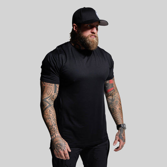 Man wearing a black t-shirt and cap with tattoos on arms against a gray background