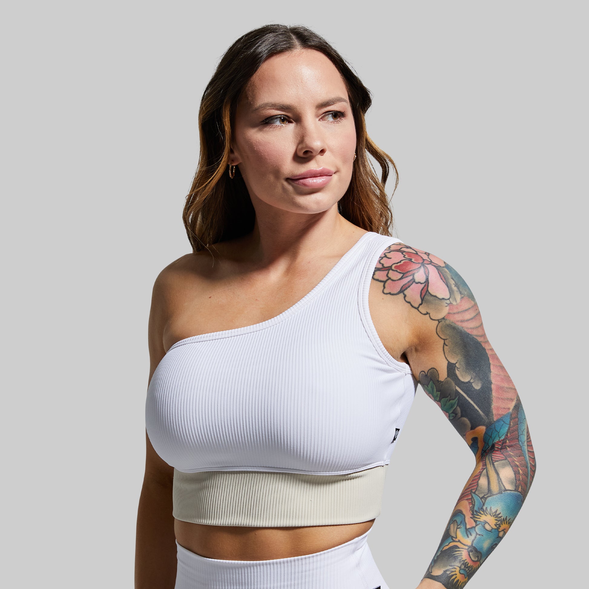 Woman wearing a white one-shoulder sports bra with a gray background
