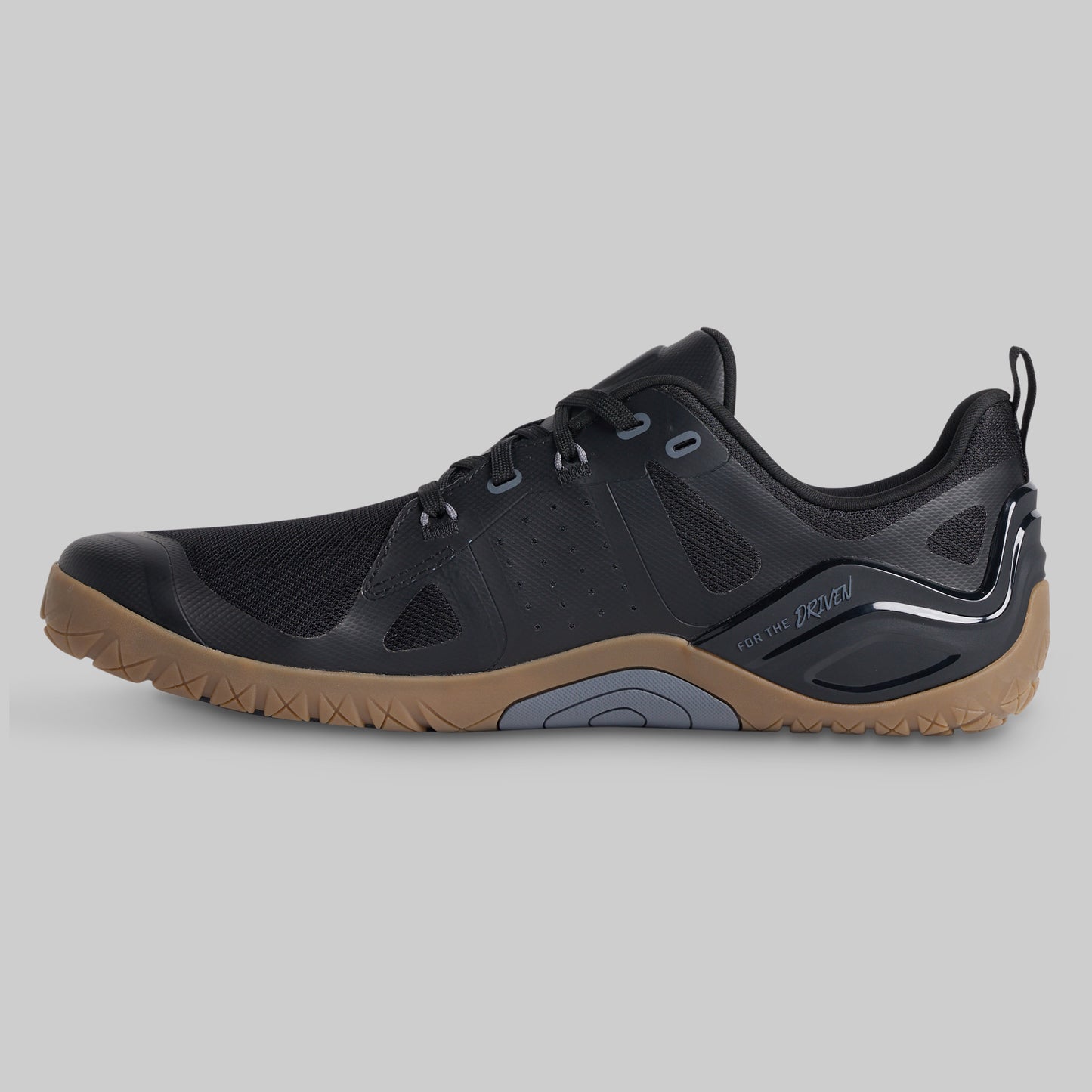 A black athletic shoe with a brown gum sole, shown in a side profile view against a solid gray background.