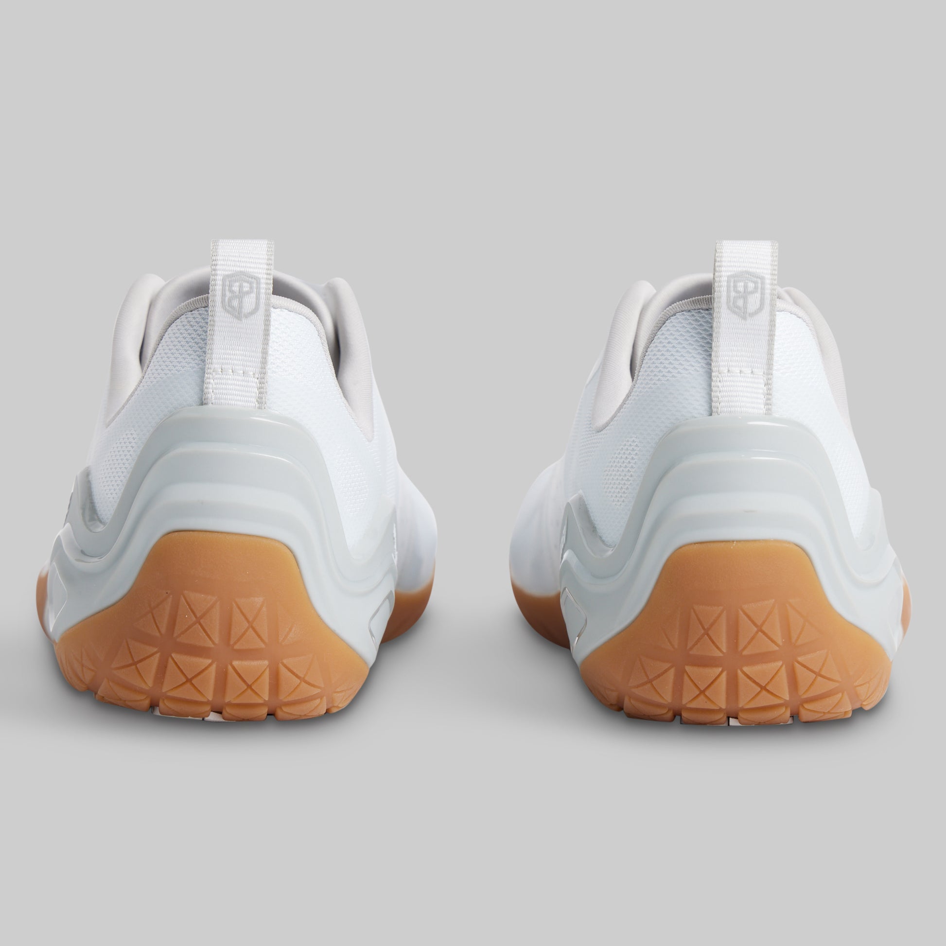 White athletic sneakers shown from the back, featuring a white mesh and synthetic upper with a light gray midsole and a gum brown textured outsole.
