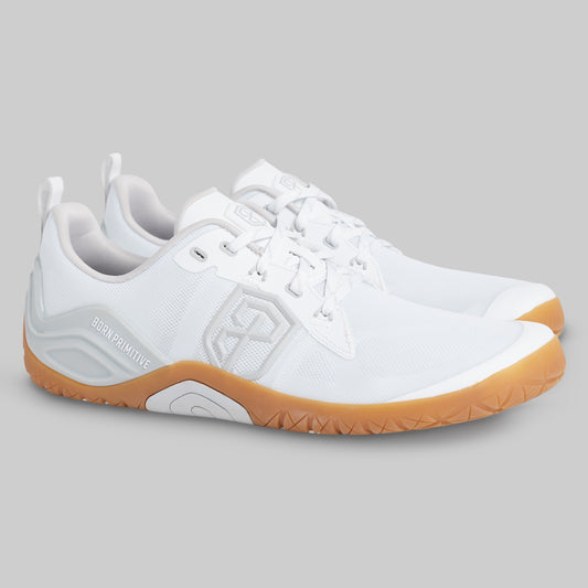 A pair of white athletic shoes with gum soles, shown from a side profile view on a solid gray background. The brand name 'BORN PRIMITIVE' is visible on the heel area.