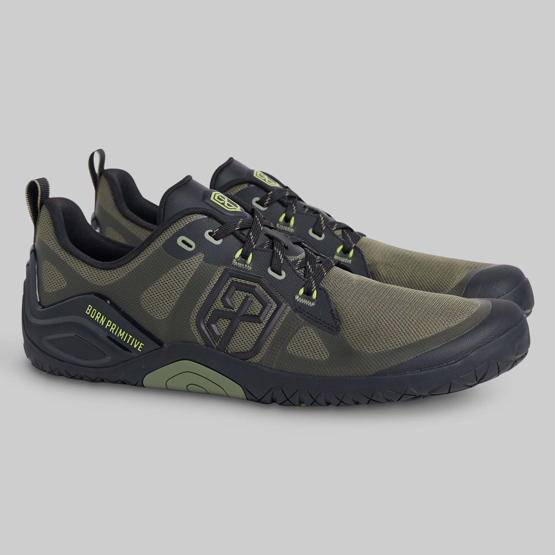 A pair of Burn Primitive minimalist shoes in olive green and black, featuring lime green accents on the laces and logo, shown against a neutral gray background.