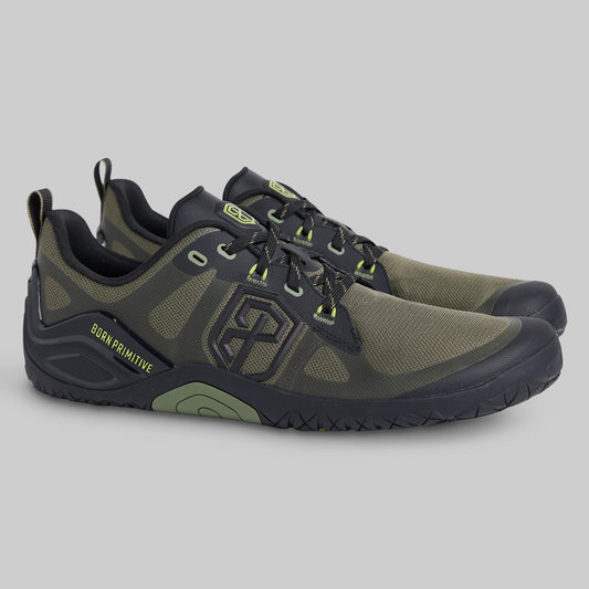 A pair of Burn Primitive minimalist shoes in olive green and black, featuring lime green accents on the laces and logo, shown against a neutral gray background.