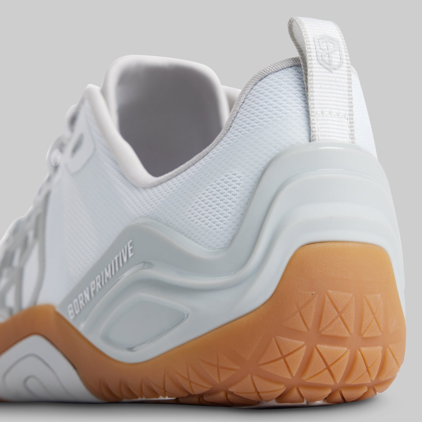 A close-up side view of a white athletic sneaker with a chunky light gray midsole and a gum brown outsole, featuring the 'BORN PRIMITIVE' branding.