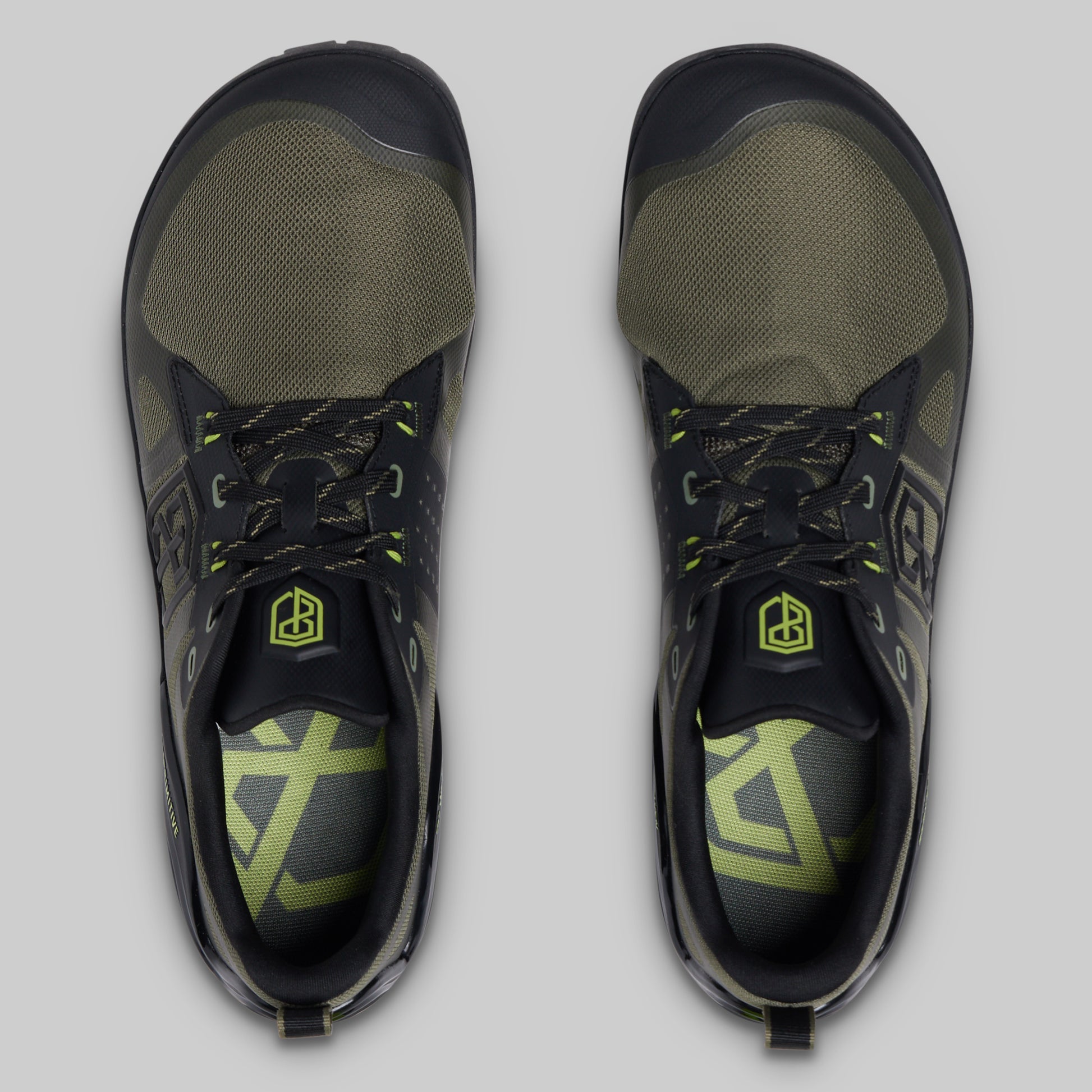 A pair of athletic minimalist training shoes shown from a top-down view on a light gray background. The shoes feature a black and olive green colorway with neon yellow-green accents on the laces, logo, and insole.