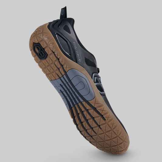 A single athletic shoe shown from a high-angle rear view, featuring a brown textured rubber sole, a dark gray and black upper, and a gray heel counter, set against a solid gray background.