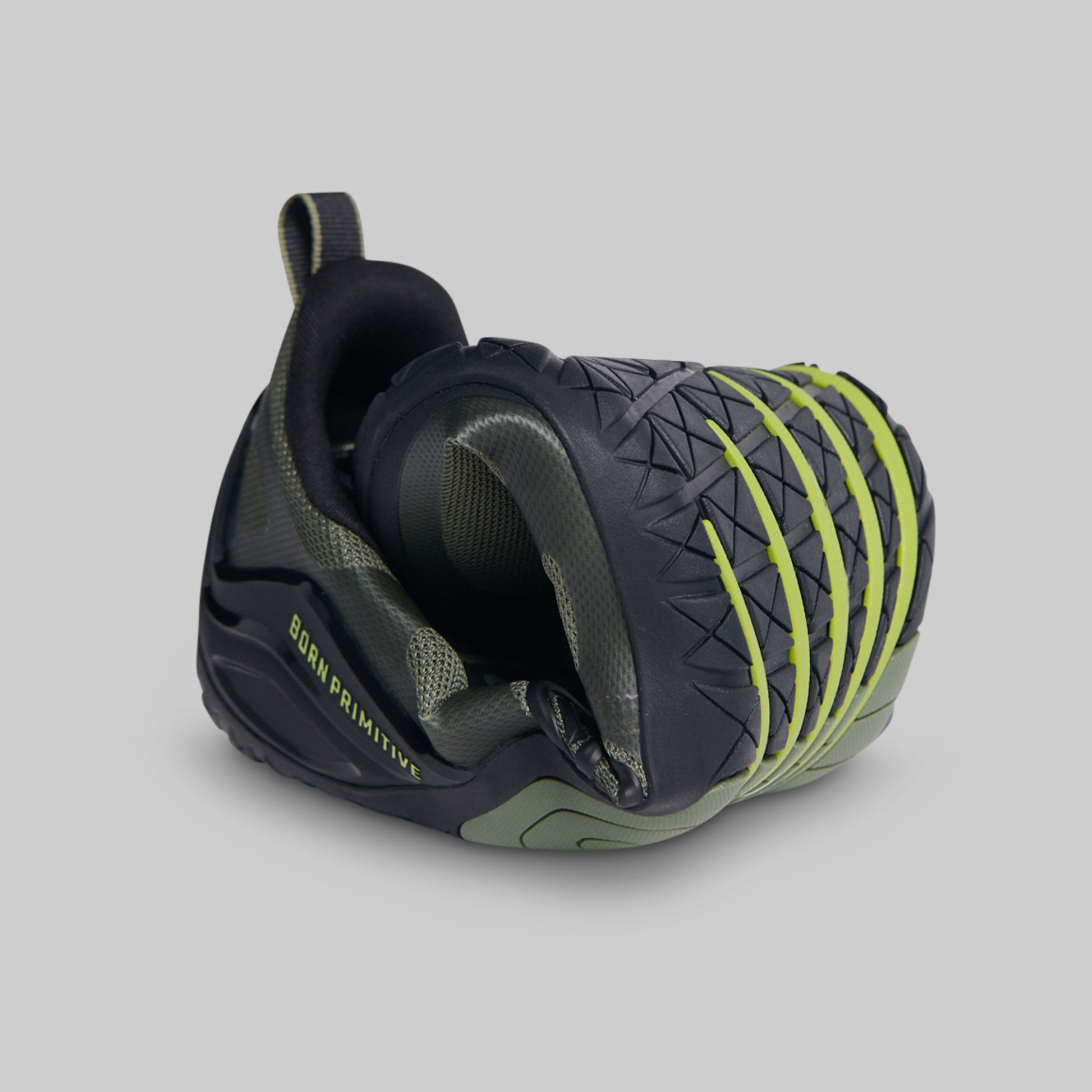 A black and green athletic barefoot shoe rolled to show flexibility against a solid gray background.