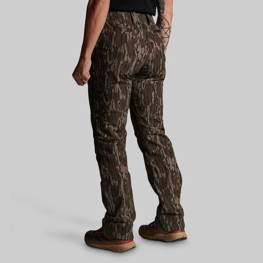 A person shown from the back wearing camouflage cargo pants, a black shirt, and brown boots against a light gray studio background.