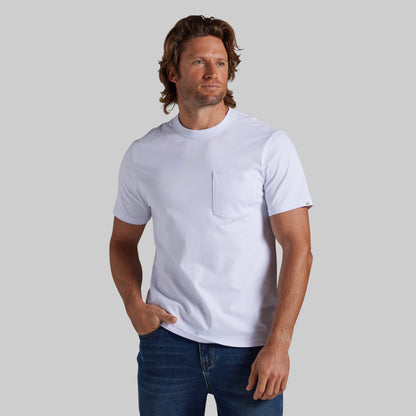A man wearing a white short-sleeve crewneck pocket t-shirt and blue jeans, standing against a solid gray studio background.