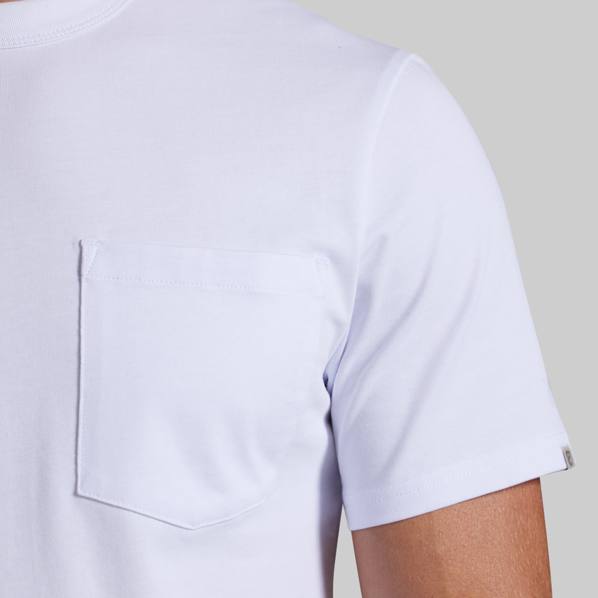 Close-up of a white short-sleeve crewneck t-shirt with a chest pocket, worn by a model against a light gray background.
