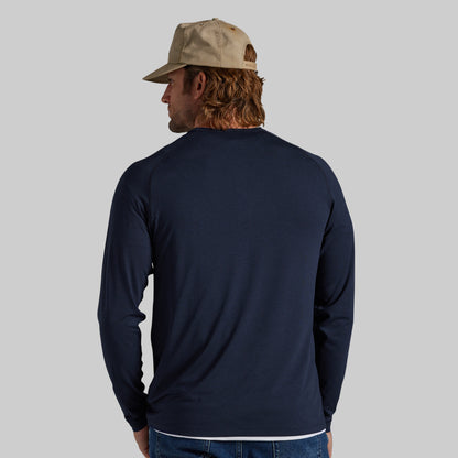 A man wearing a navy blue long-sleeve shirt and a beige baseball cap, shown from the back against a solid gray background.