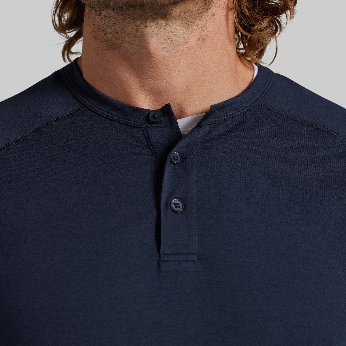 Close-up of a man wearing a navy blue henley shirt with a three-button placket, showing the collar, fabric texture, and part of his neck and chin against a light gray background.