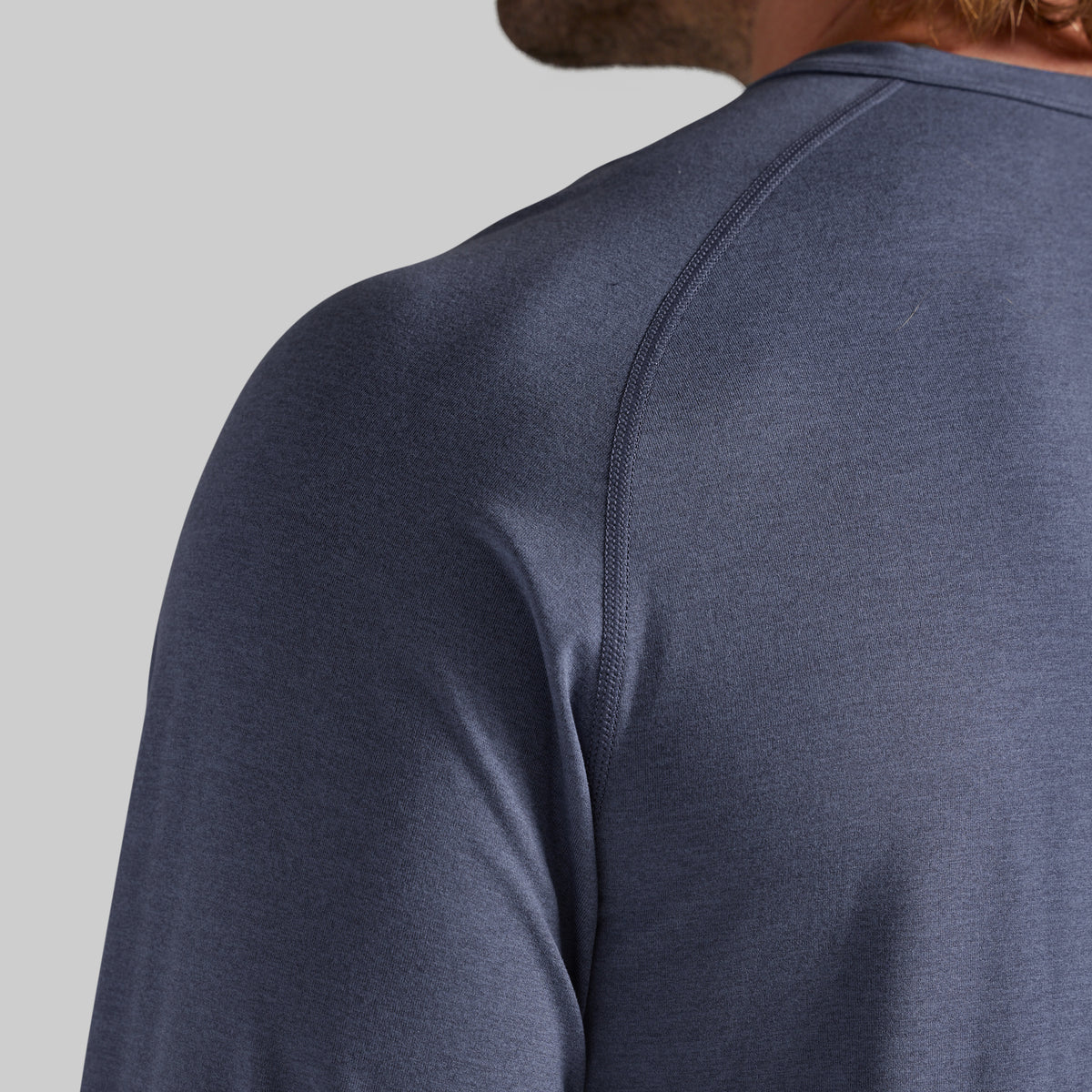 Close-up back view of a person wearing a heathered slate blue long-sleeve athletic shirt, showing the shoulder seam and neck area against a light gray background.