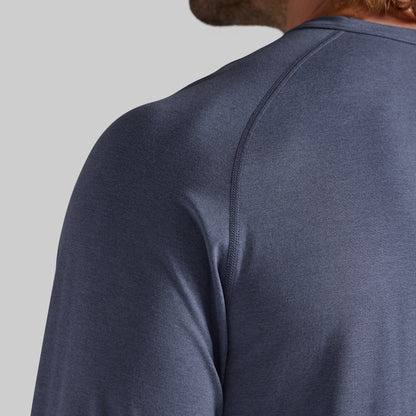 Close-up back view of a person wearing a heathered slate blue long-sleeve athletic shirt, showing the shoulder seam and neck area against a light gray background.