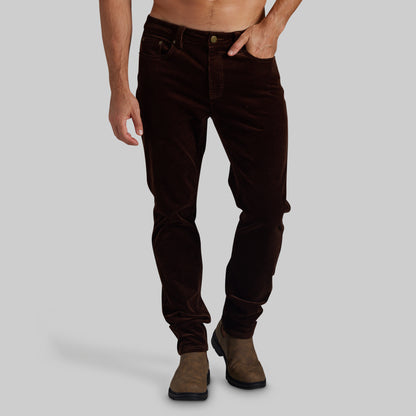 A person modeling dark brown corduroy pants with brown suede boots against a solid gray studio background.