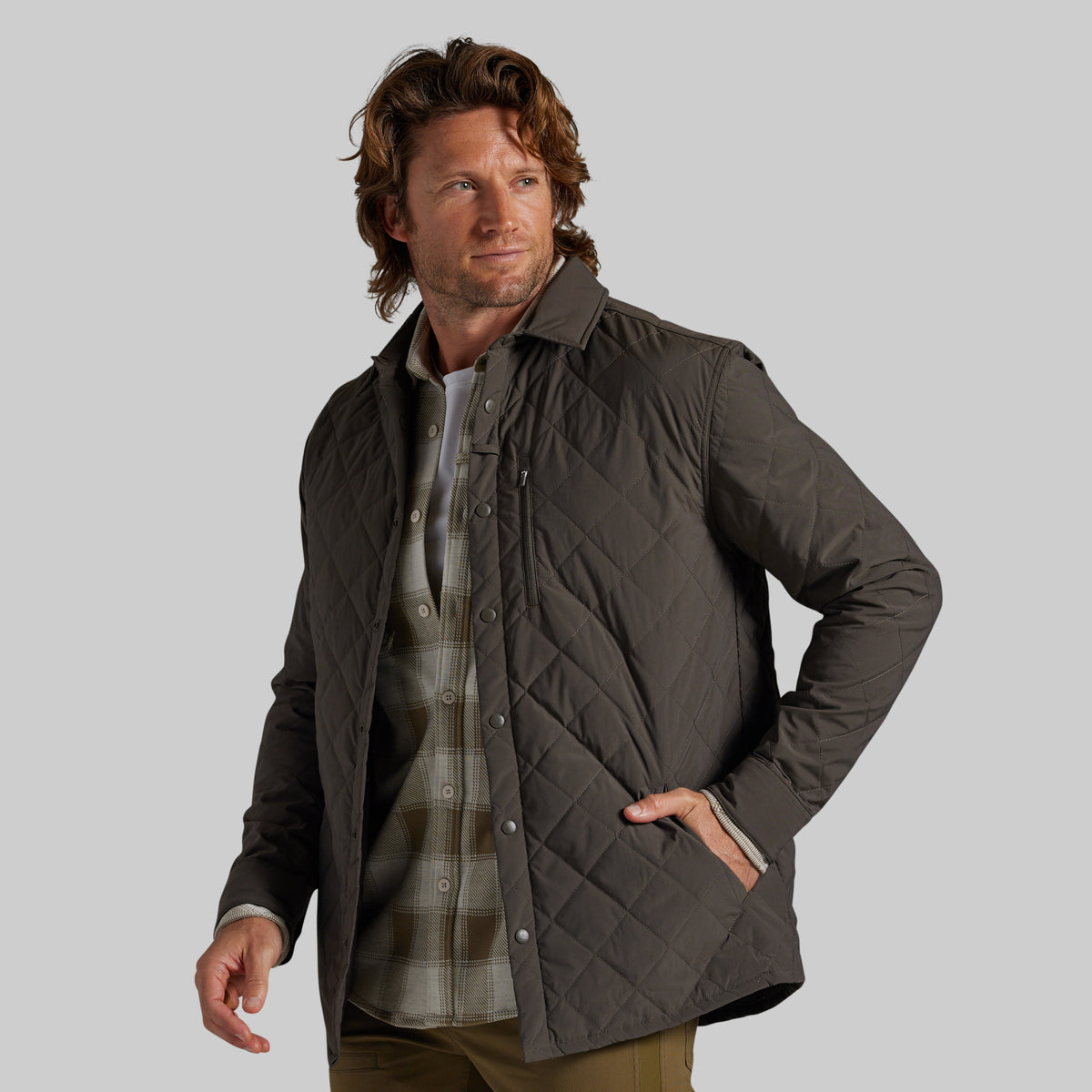A man wearing a dark brown diamond-quilted jacket over a plaid shirt, photographed against a solid light gray background.