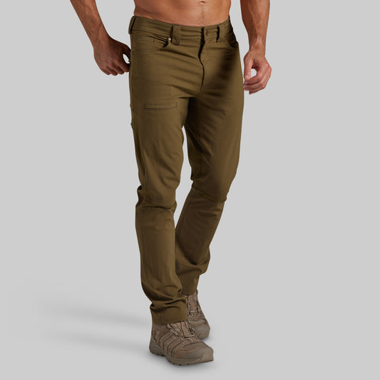 A man wearing olive green pants and brown hiking boots, shown from the waist down against a solid gray background.