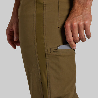 Close-up of a person wearing olive green pants, showing a side pocket with a gray smartphone partially tucked inside, against a light gray background.