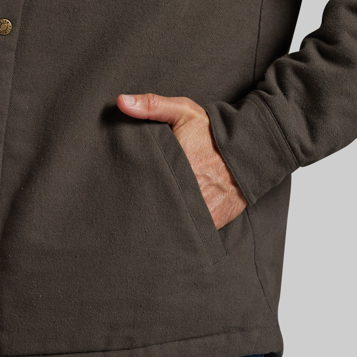 Close-up of a person wearing a dark brown wool-blend jacket, showing a hand tucked into a front pocket.