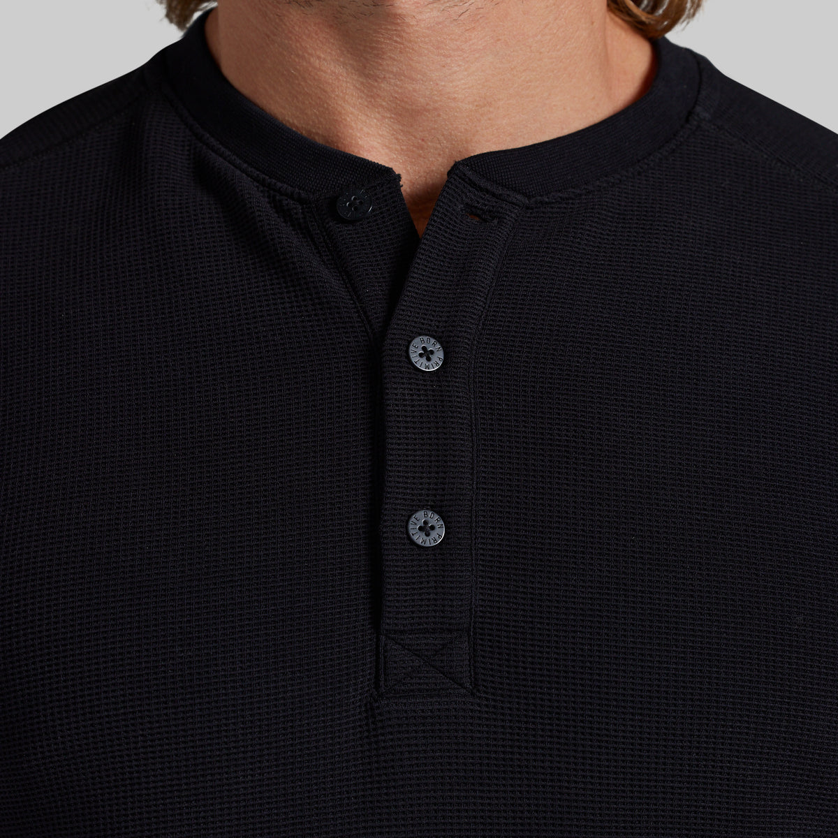 Close-up of a person wearing a black waffle-knit henley shirt with a button placket and a short stand collar.