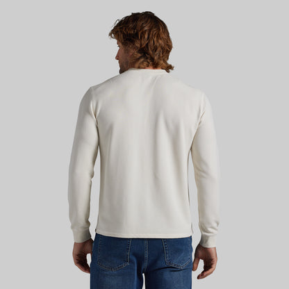 A man viewed from behind wearing a plain off-white long-sleeve crewneck sweater and blue jeans, set against a solid light gray background.